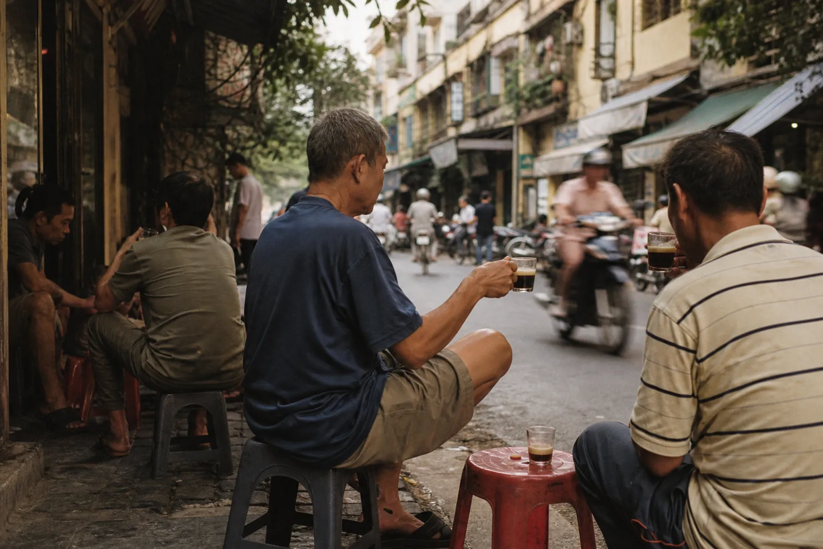 KI-generiert: Hà Nội Altstadt, niedrige Plastikhocker am Gehweg, Menschen mit Gläsern, Motorroller verschwommen