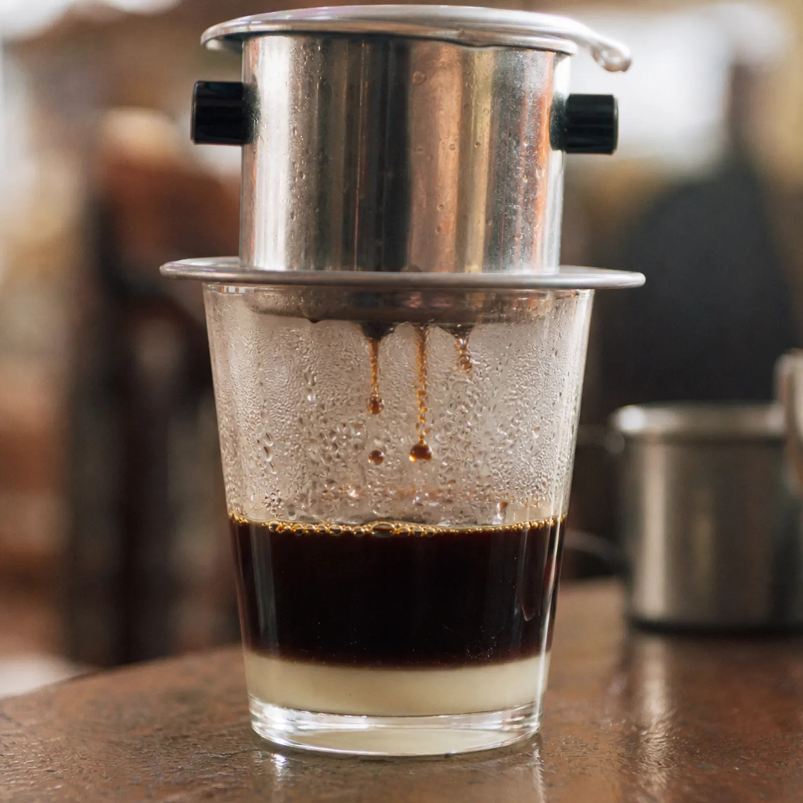 KI-generiert: Makroaufnahme, Kaffee tropft aus einem Phin in ein Glas mit Kondensmilchschicht