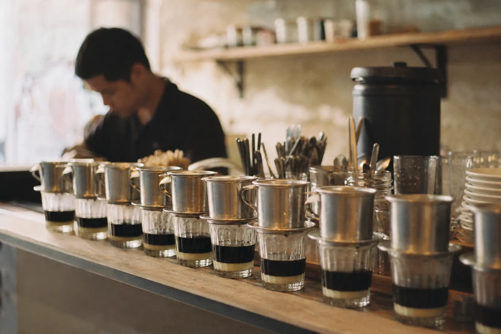KI-generiert: Sài Gòn am Morgen, Phin-Filter stehen in einer Reihe auf der Theke eines Cafés